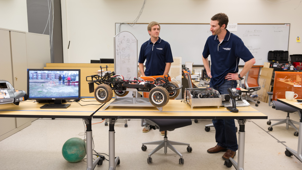 Two individuals working on a small vehicle in a lab