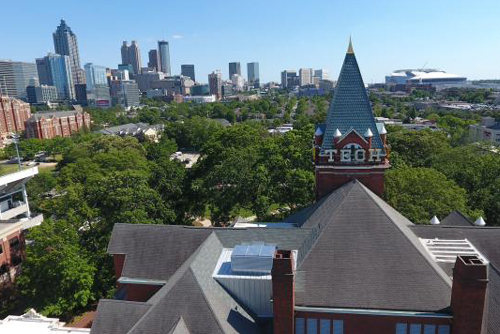 Aerial view of Georgia Tech’s Tech Tower rising above campus trees, with the Atlanta skyline and surrounding buildings visible in the background.