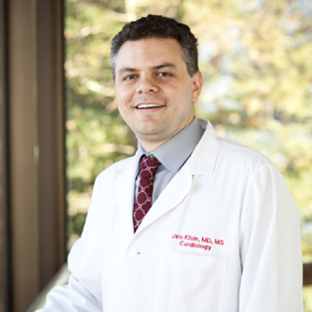 man wearing a white lab coat standing in front of foilage