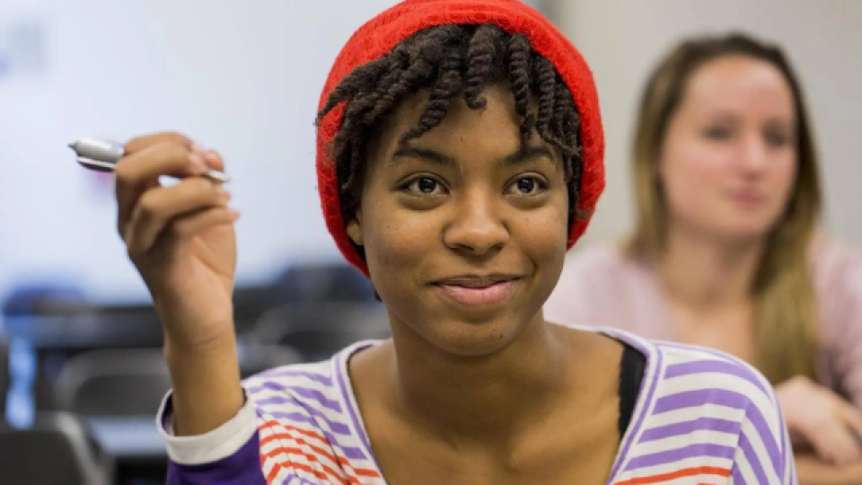 Student in a classroom holding a pen